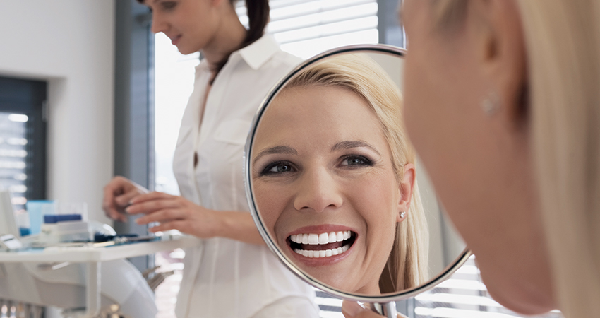 Woman looks at her dental veneers in mirror